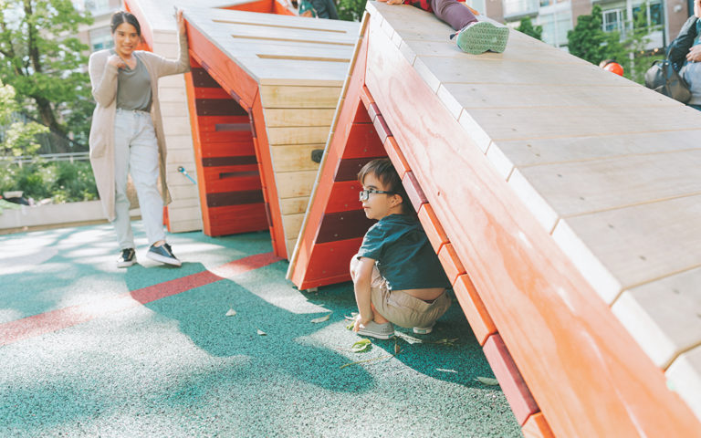 Boy hides under accessible playground in Vancouver ribbon climber sculpture hide and seek