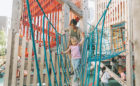 Girl and her mom cross giant rope bridge between timber tower at inclusive playground at Smithe and Richards