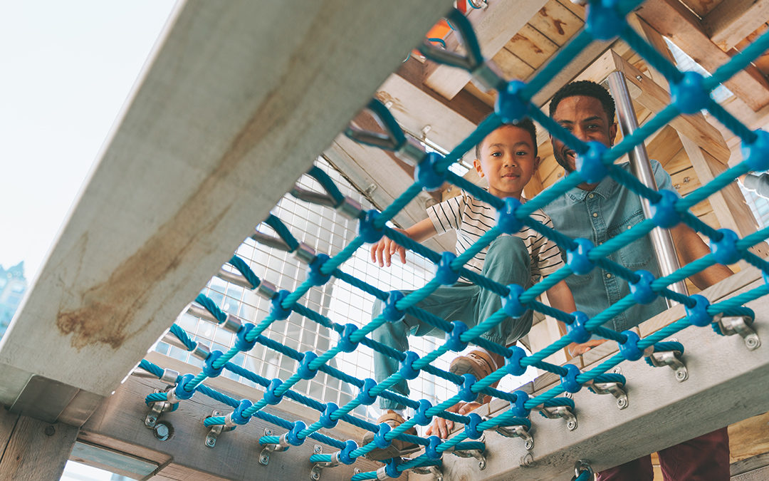 Father and son look down through net in Vancouver timber playground tower