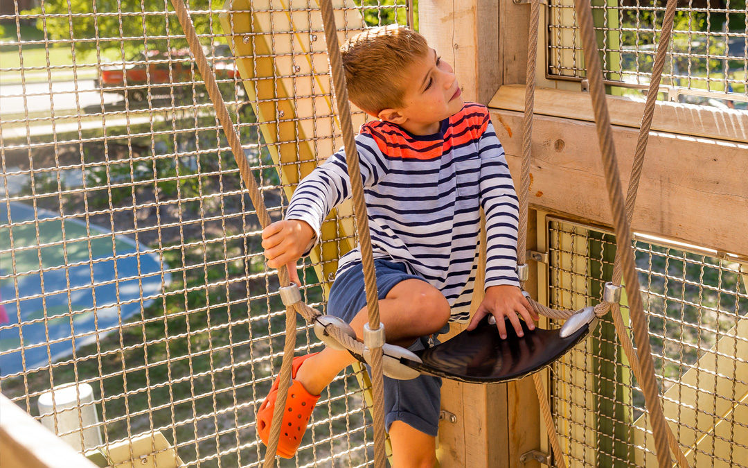 Child sits in sling seat inside John Ball Zoo playground tower