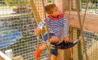 Child sits in sling seat inside John Ball Zoo playground tower