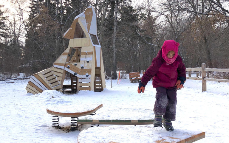 Child plays in winter on wobble board at Sir Wilfrid Laurier howling coyote playground in Edmonton